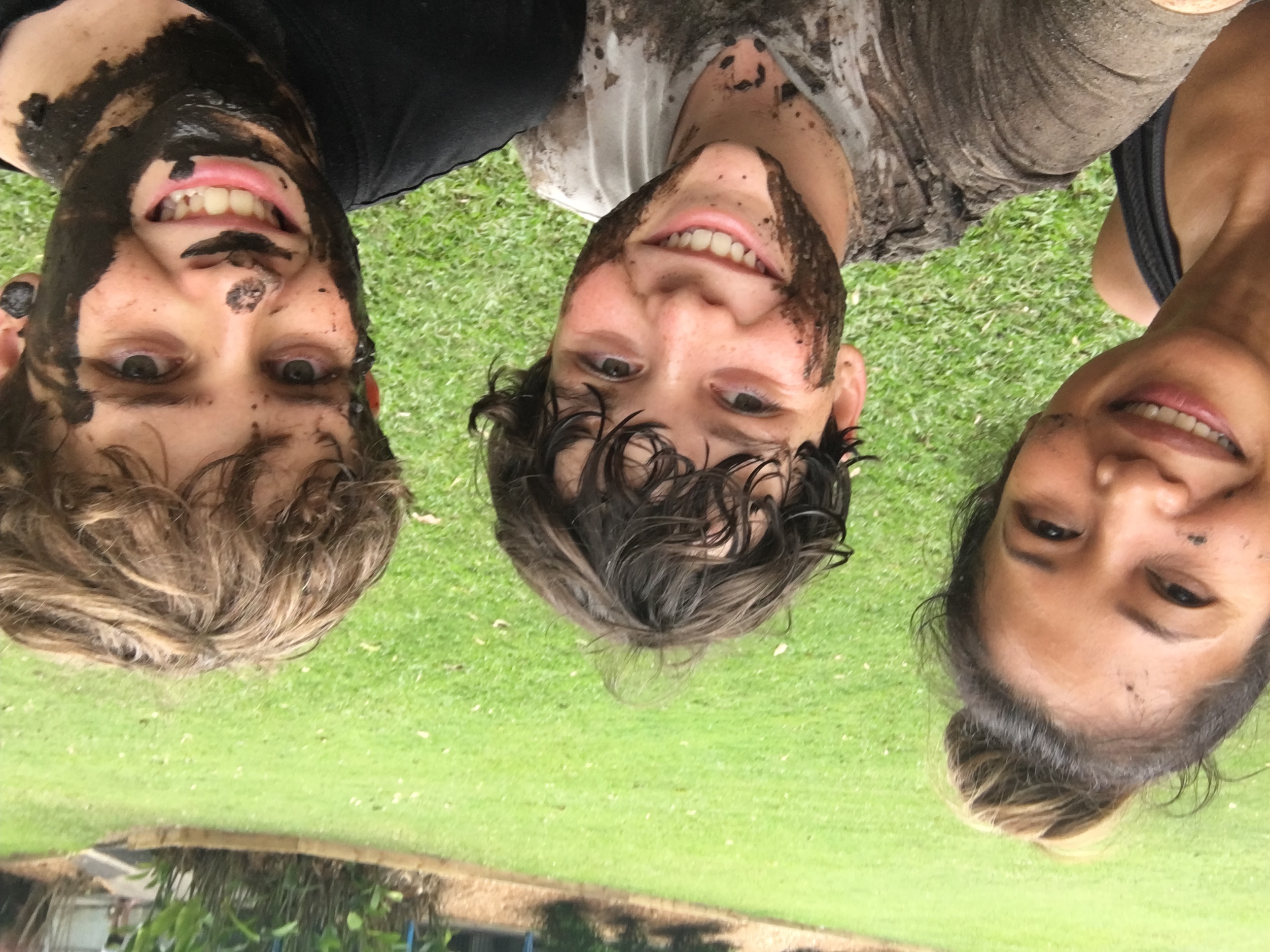 Group selfie of students and an adult outdoors with muddy faces during a camp activity.